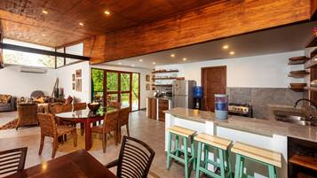 A modern kitchen with a central island, built-in appliances, and a dining area with wicker chairs.