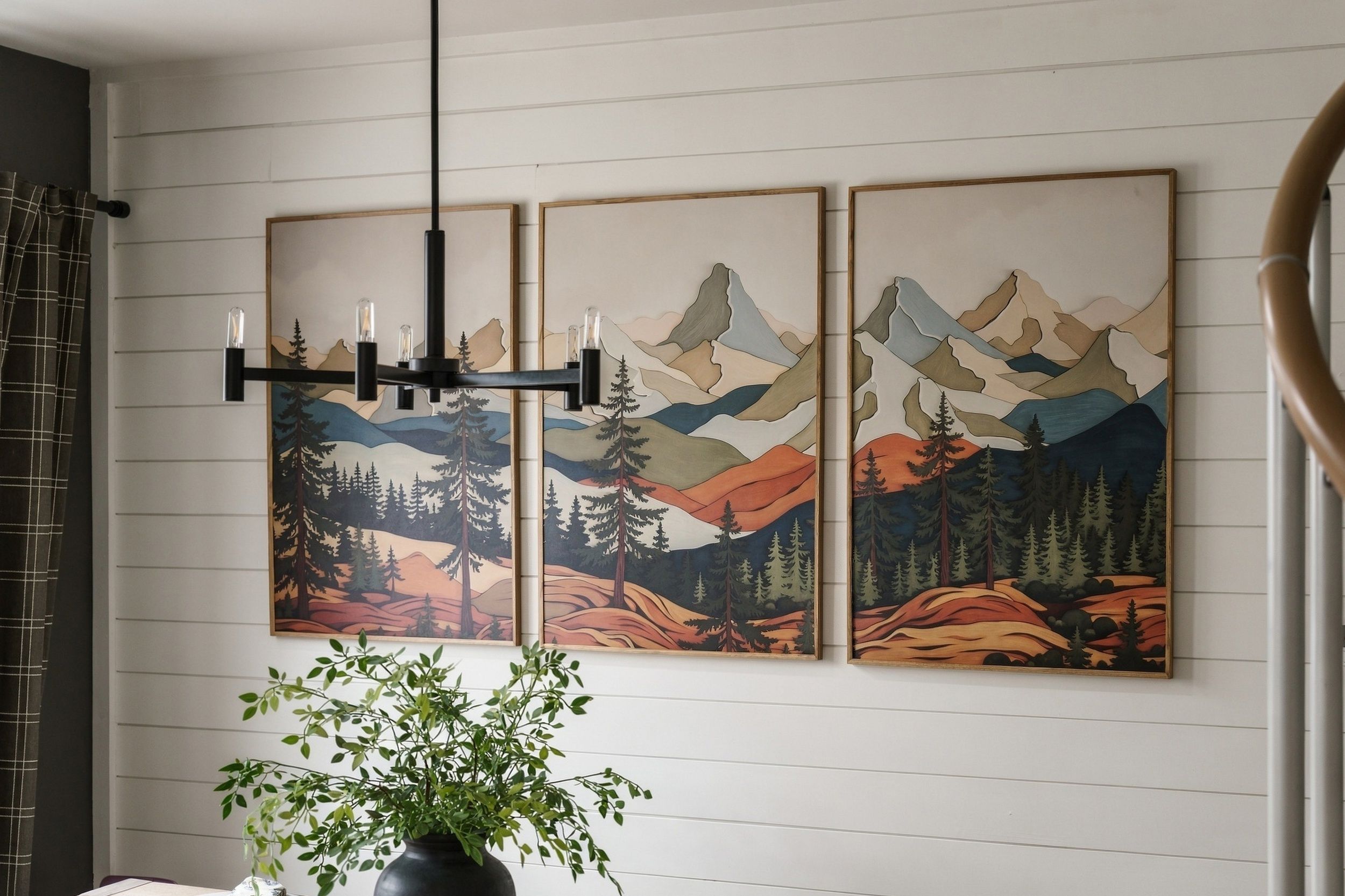 A room with a large wall-mounted painting of a mountainous landscape, a black chandelier, and a potted plant.