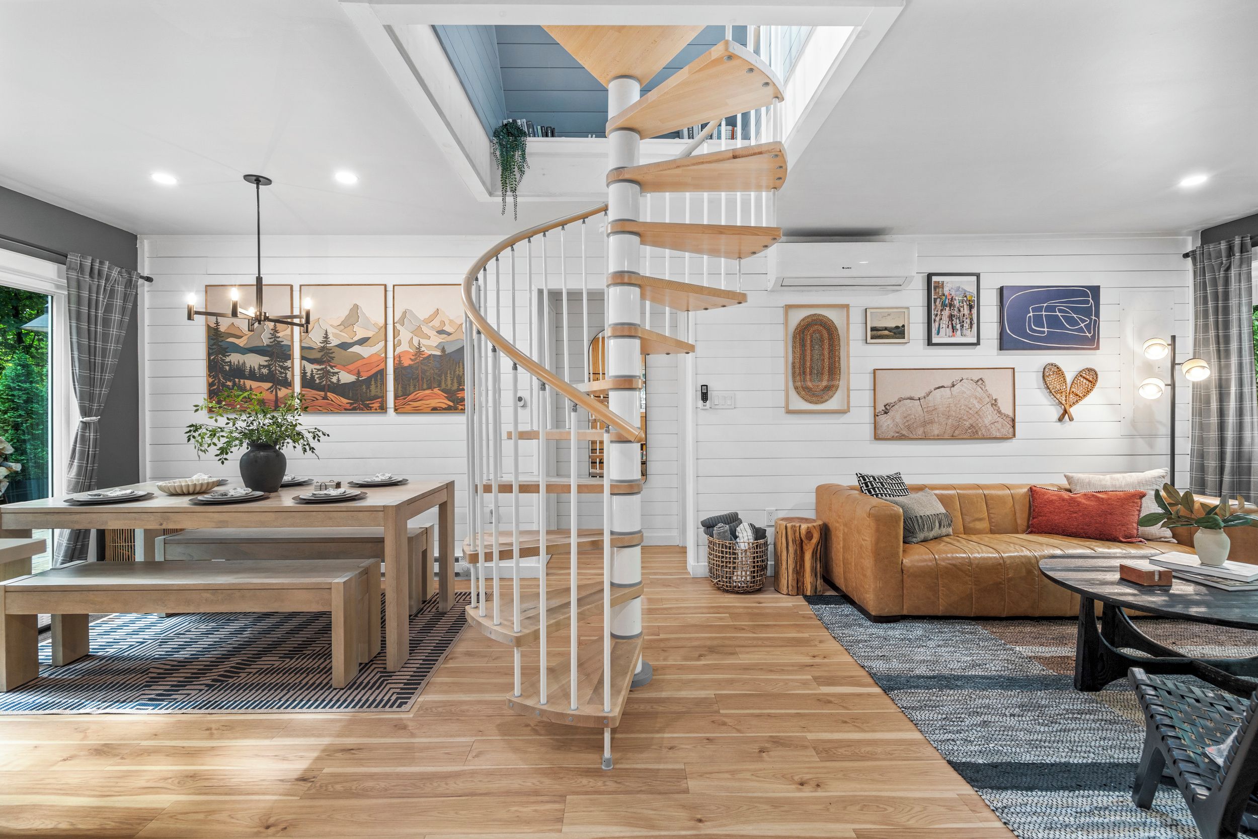 A modern living space with a spiral staircase, a dining area, a sofa, and artwork on the walls.