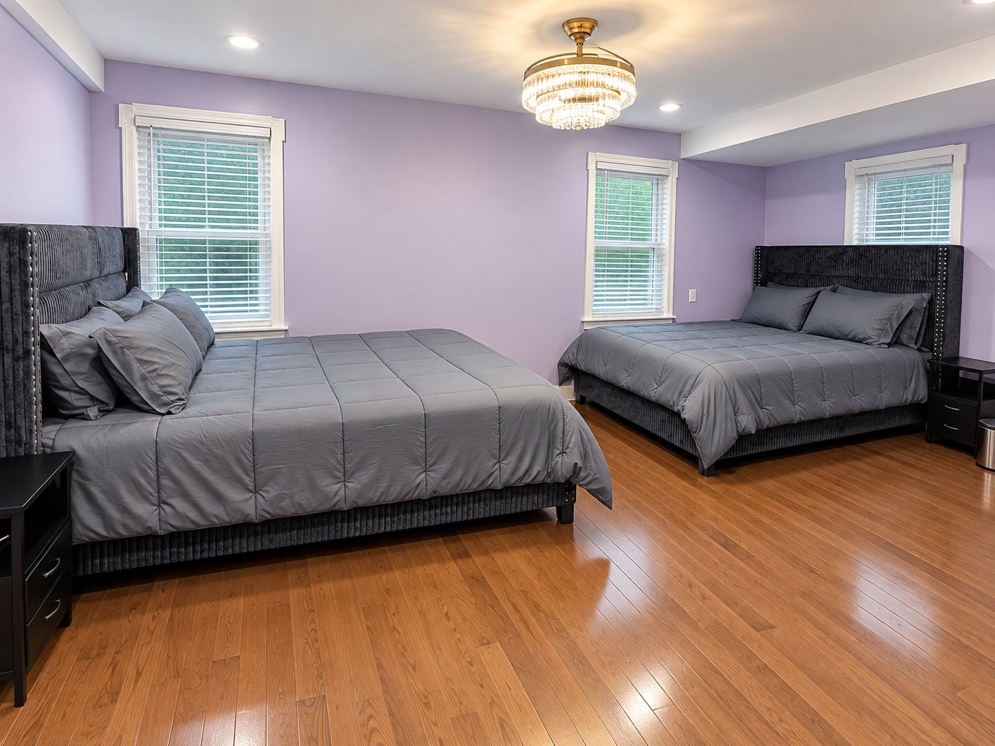 A bedroom with two beds, wooden flooring, and a chandelier.