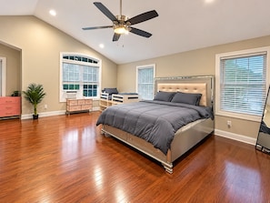 A bedroom with a bed, a desk, a chair, a dresser, and a ceiling fan.