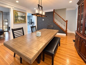 Un comedor con una mesa de madera, sillas, un banco, una araña y una escalera.