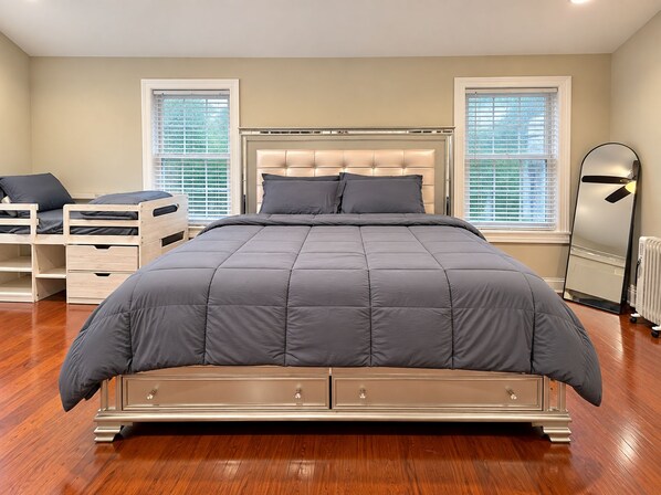 Un dormitorio con una cama grande, una mesita de noche, un aparador y dos ventanas con persianas.