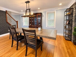 A dining area with a wooden table, dark chairs, a chandelier, a wooden cabinet, and a bookshelf against a wall.