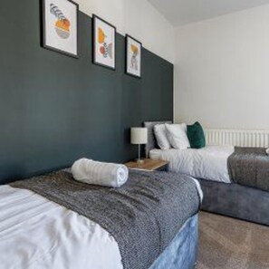 A hotel room with a bed, a nightstand, a lamp, and a wall with framed pictures. - Stockton-on-tees - Sleeps 4 - Near Norton Village (Stockton-on-Tees)