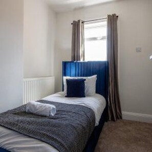 A single bed with a blue headboard, white bedding, and a grey blanket. - Stockton-on-tees - Sleeps 4 - Near Norton Village (Stockton-on-Tees)