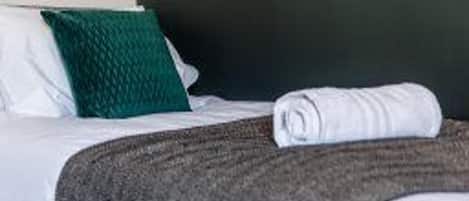 Una cama bien hecha con un almohadón verde y una toalla blanca enrollada.