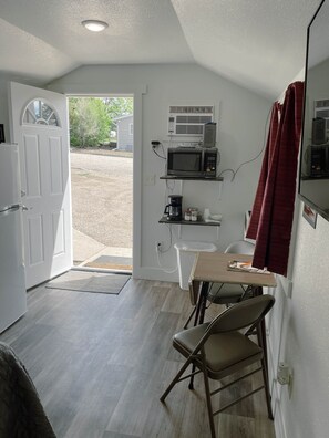 A compact kitchen with a microwave, coffee maker, and a small dining table with a chair.