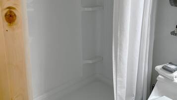 A shower enclosure with a white curtain, a white toilet, and a wooden door.