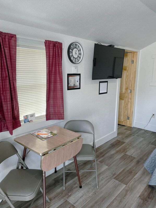 A room with a table, two chairs, a clock, a television, and a door.