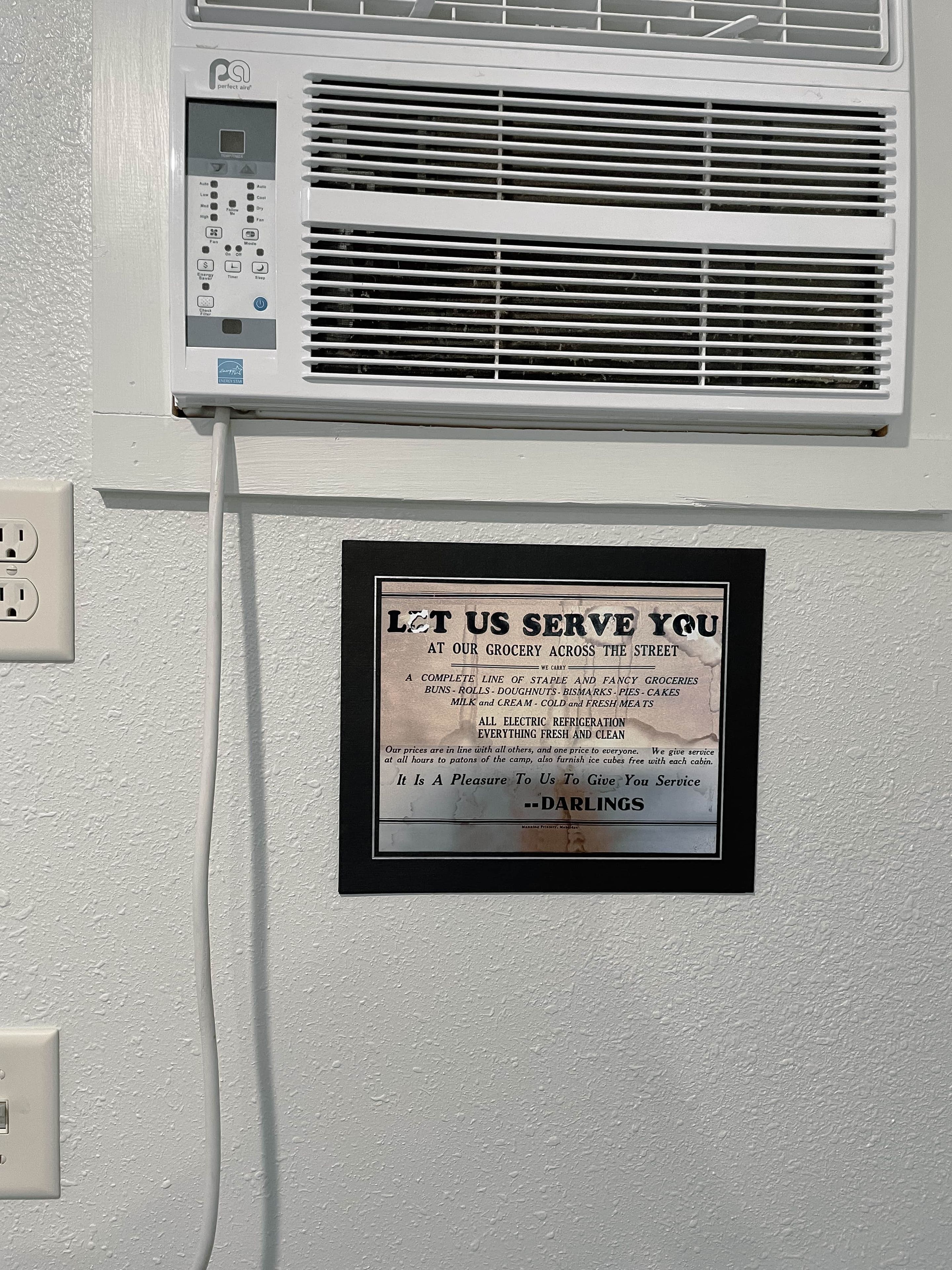 Un climatiseur mural, doté d’un panneau de commande et d’une enseigne publicitaire pour des services d’épicerie.