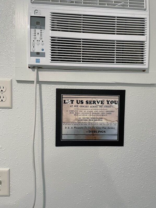 A wall-mounted air conditioning unit with a control panel and a sign advertising grocery services.