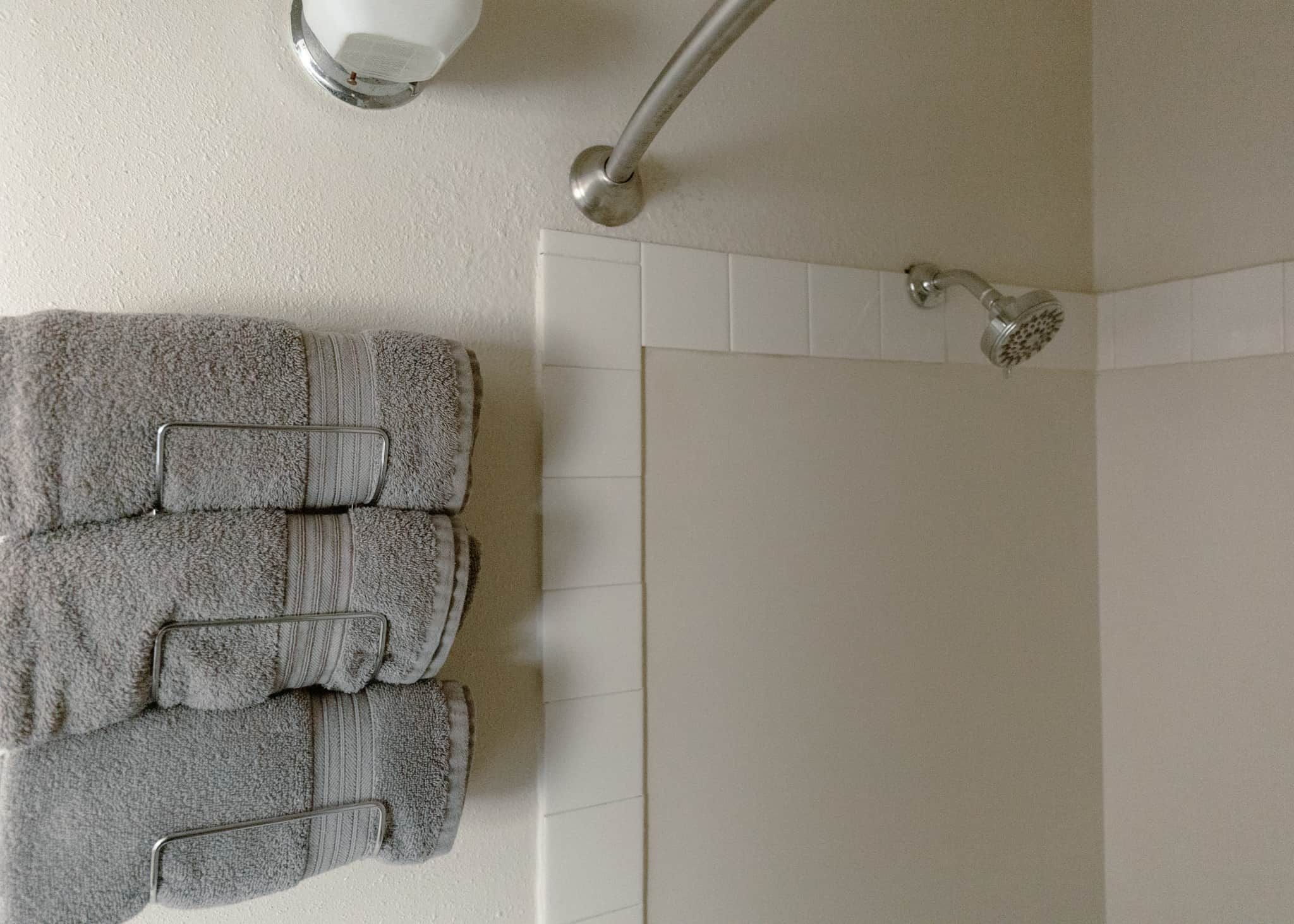 A bathroom with a shower, a towel rack with folded towels, and a wall-mounted light fixture.