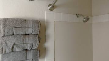 A bathroom with a shower, a towel rack with folded towels, and a wall-mounted light fixture.