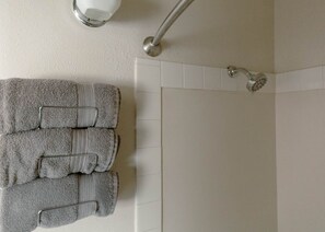 A bathroom with a shower, a towel rack with folded towels, and a wall-mounted light fixture.