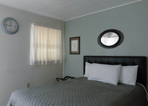 Un dormitorio con cama, un reloj de pared, una ventana con cortinas, un mapa enmarcado y un espejo redondo.