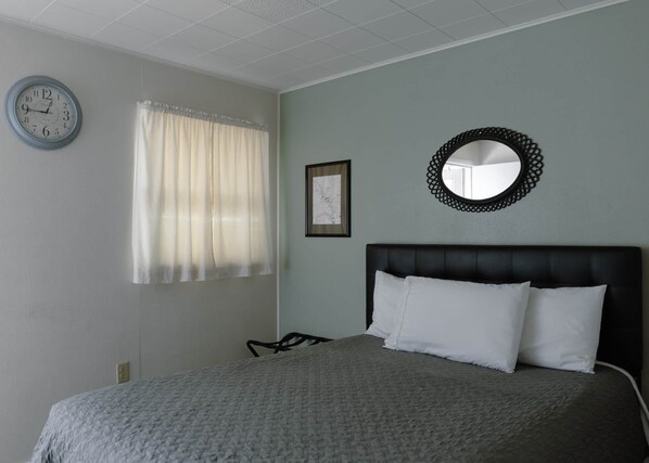 Une chambre à coucher avec un lit, une horloge murale, une fenêtre avec des rideaux, une carte encadrée et un miroir rond.