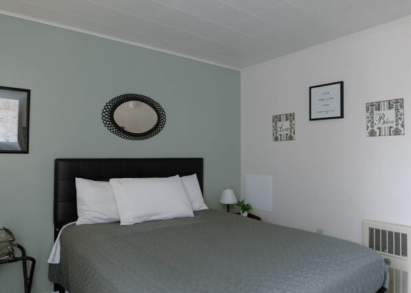 A bedroom with a bed, a round mirror, and several framed pictures on the wall.