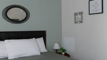 Un lit bien fait, avec des oreillers blancs et une couvre-lit grise, dans une pièce dont le plafond et les murs sont blancs.
