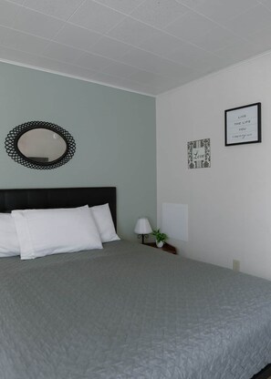 Un lit bien fait, avec des oreillers blancs et une couvre-lit grise, dans une pièce dont le plafond et les murs sont blancs.