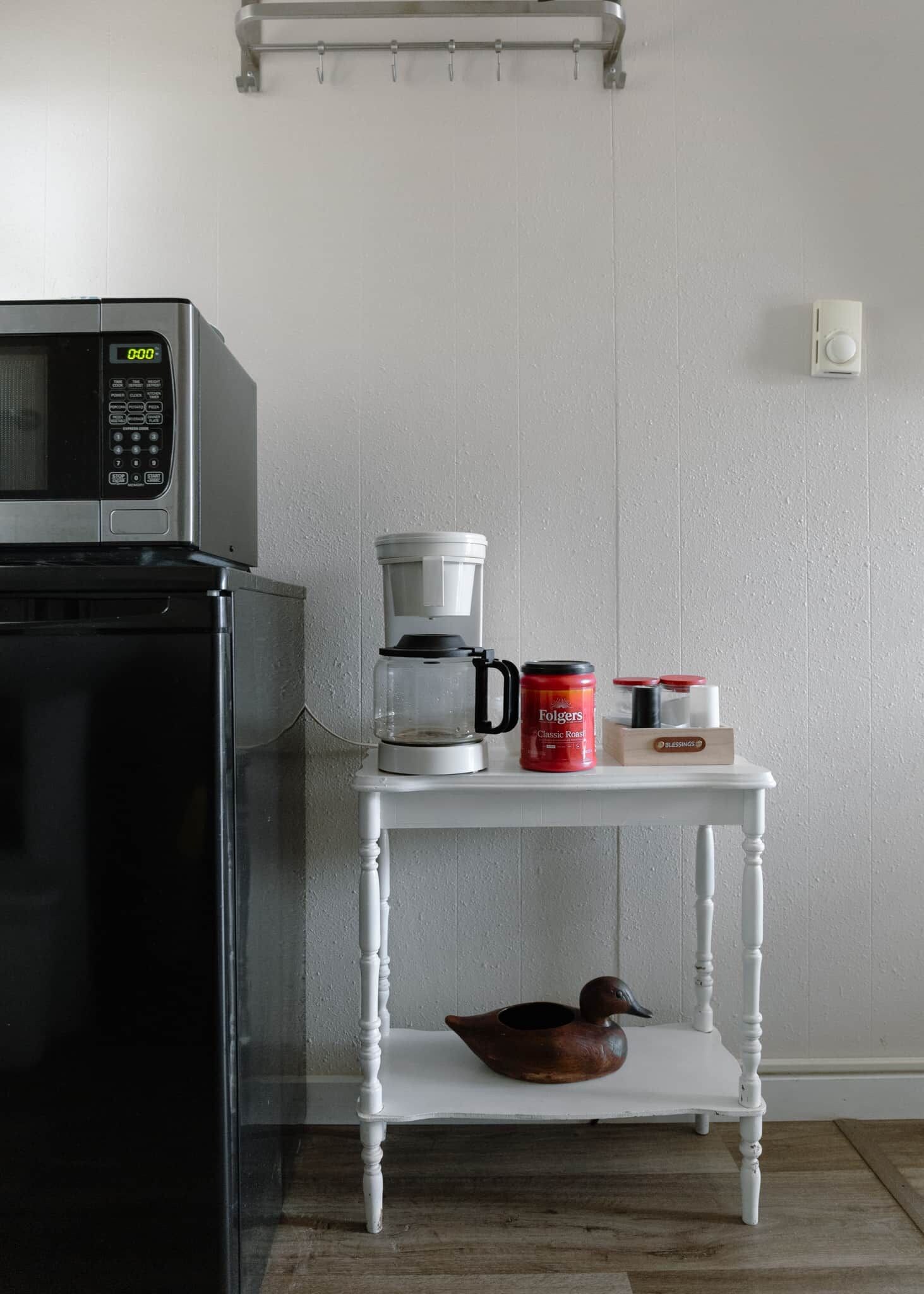 A kitchen with a microwave, coffee maker, and a shelf with a duck and coffee containers.