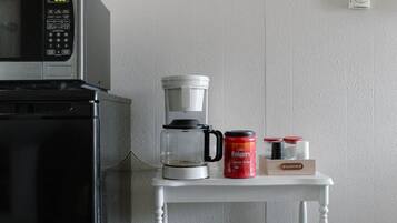 A kitchen with a microwave, coffee maker, and a shelf with a duck and coffee containers.