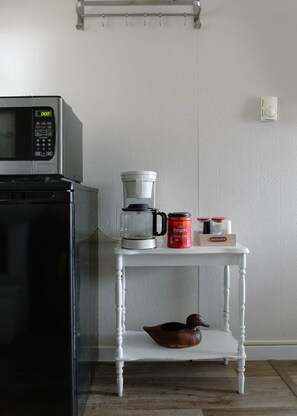 Une cuisine équipée d’un four à micro-ondes, d’une machine à café et d’une étagère où sont posés un canard décoratif et des récipients à café.