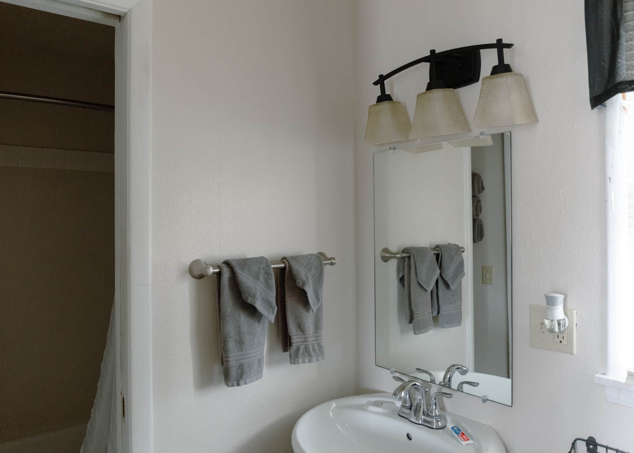 A bathroom with a white sink, two towel racks with towels, a mirror, and a light fixture above the mirror.