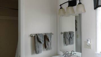 A bathroom with a white sink, two towel racks with towels, a mirror, and a light fixture above the mirror.