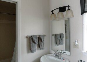 Une salle de bain avec un lavabo blanc, deux porte-serviettes avec des serviettes, un miroir et un luminaire placé au-dessus du miroir.