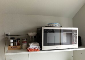 Eine Küche mit einer weißen Mikrowelle auf einem Regal, einem Gewürzregal und einem Mehlbehälter.