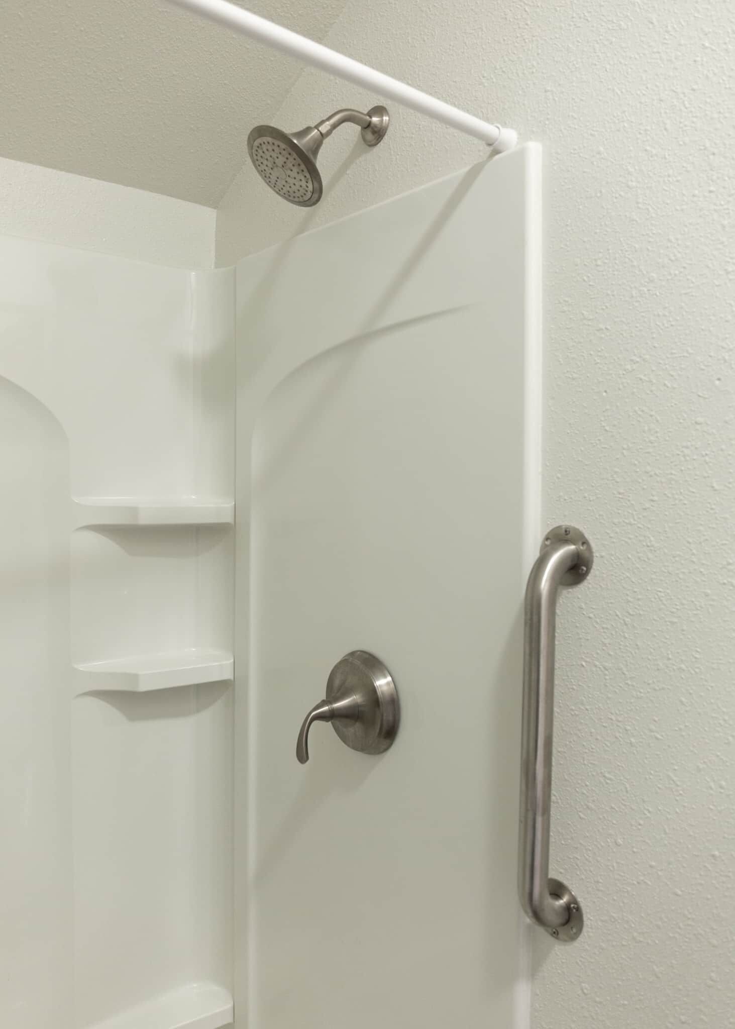A shower enclosure with a handheld showerhead, a door with a lever handle, and a grab bar on the right side.