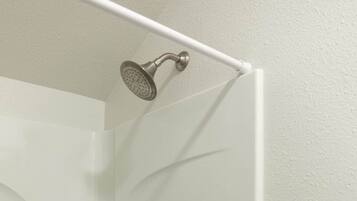 A shower enclosure with a handheld showerhead, a door with a lever handle, and a grab bar on the right side.