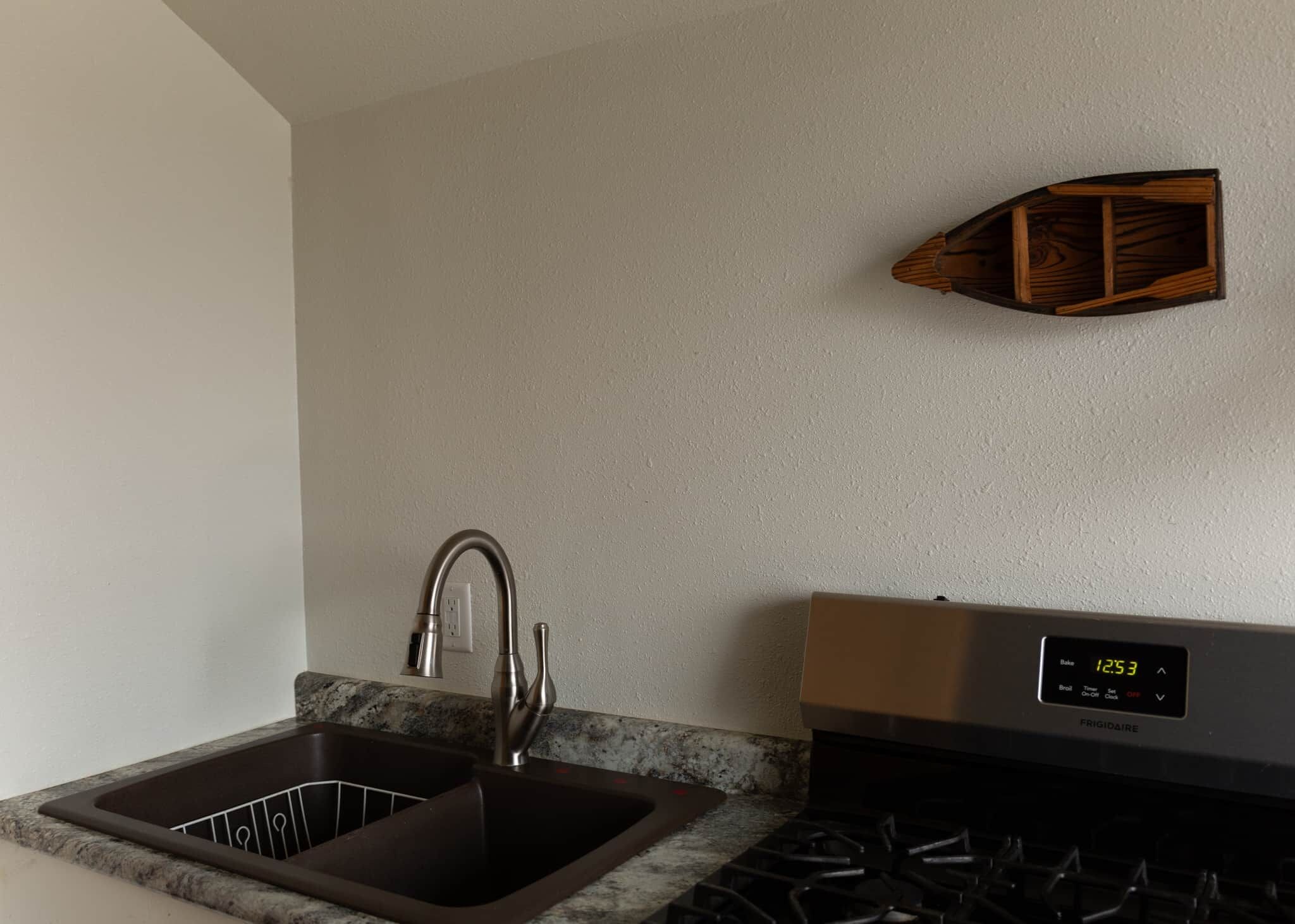A kitchen with a stainless steel sink, a built-in oven, and a wall-mounted clock.