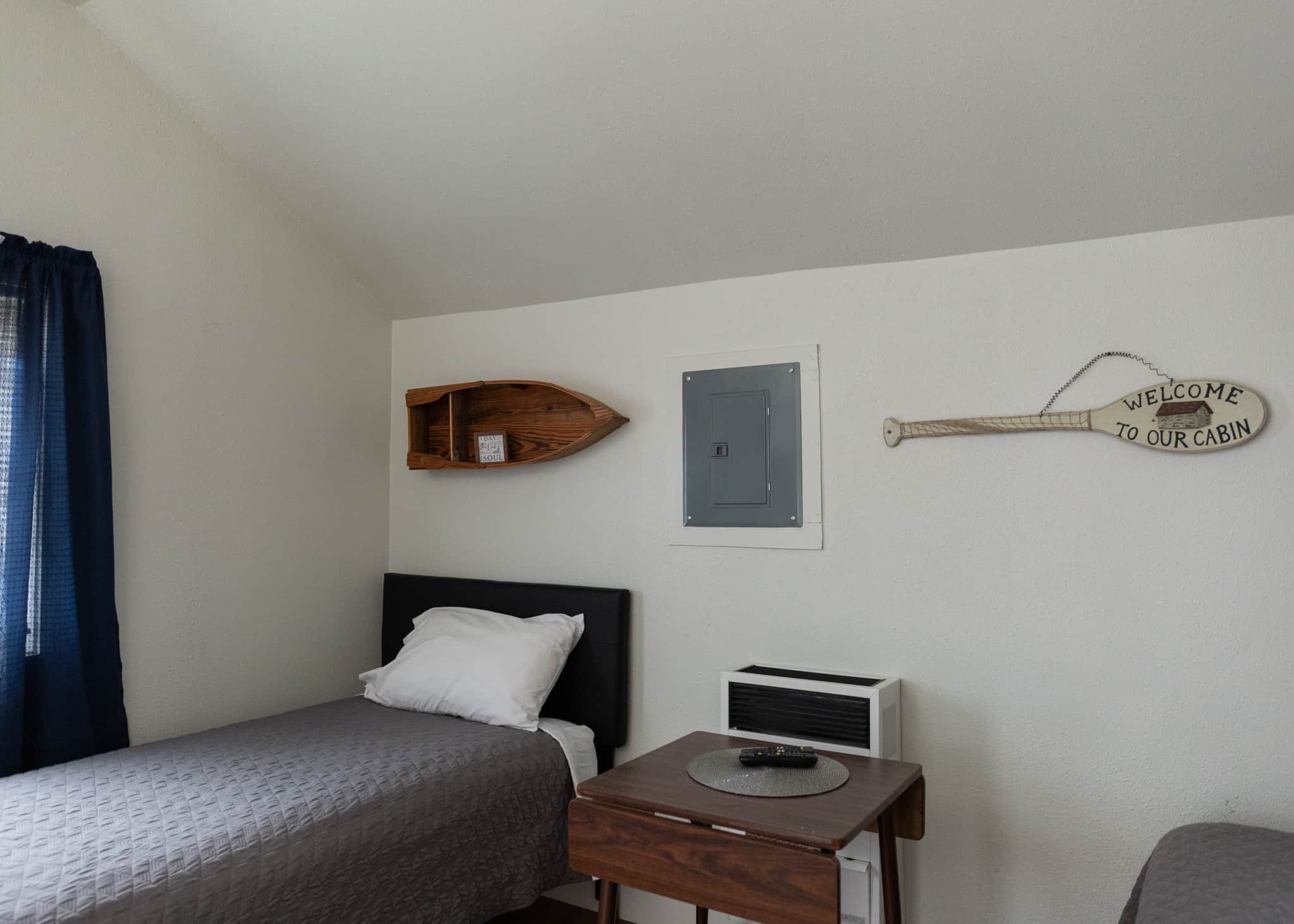 A bedroom with two beds, a wooden shelf, a wall-mounted heater, and a welcome sign.