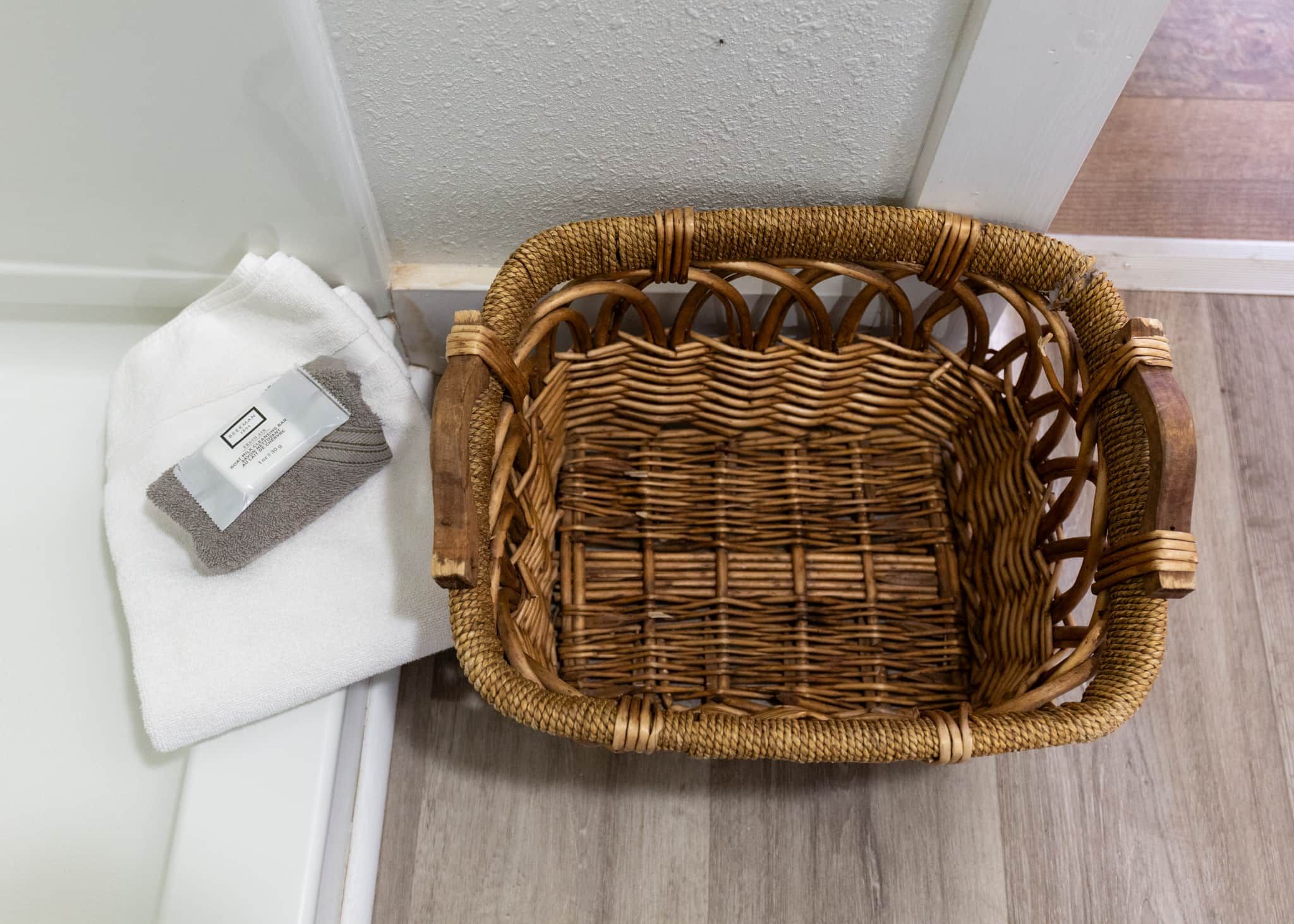 A wicker basket next to a white towel and a bar of soap on a white surface.