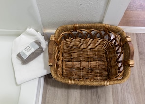 A wicker basket next to a white towel and a bar of soap on a white surface.