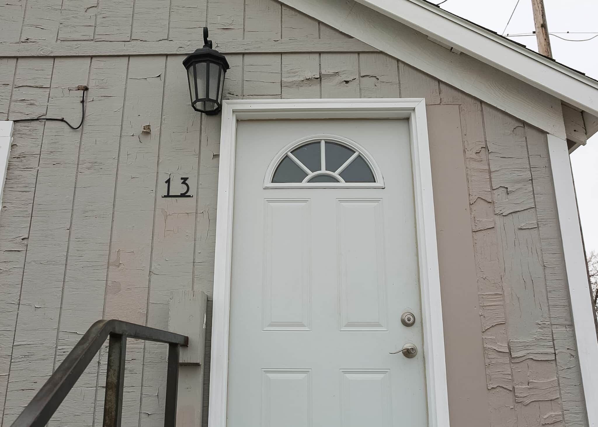 A white door with a window above it, a number '13' on the wall, and a black metal railing.