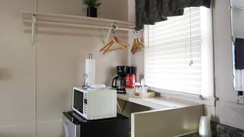 Una kitchenette compacta con microondas, cafetera y refrigerador pequeño.