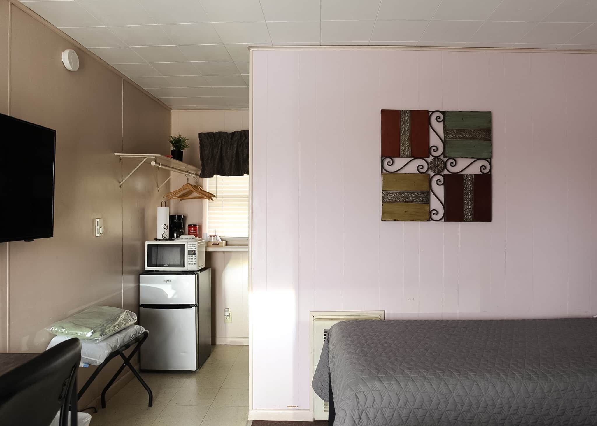 Habitación compacta con cama, escritorio, kitchenette y televisor.