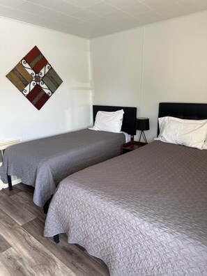 A hotel room with two beds, a wall-mounted artwork, and a bedside table with a lamp.