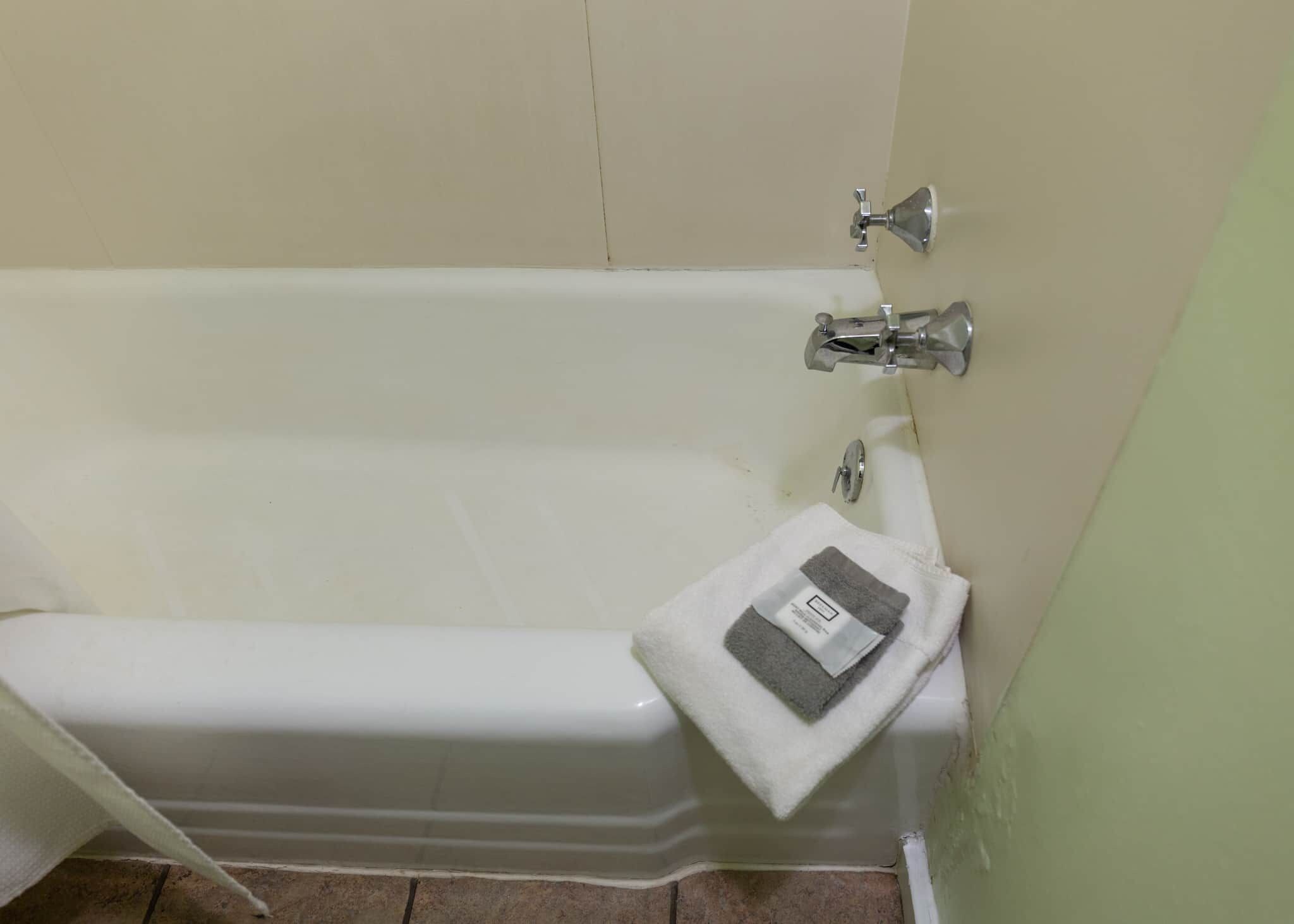 Una bañera con una toalla al lado, un cabezal de ducha y un grifo instalado en la pared.