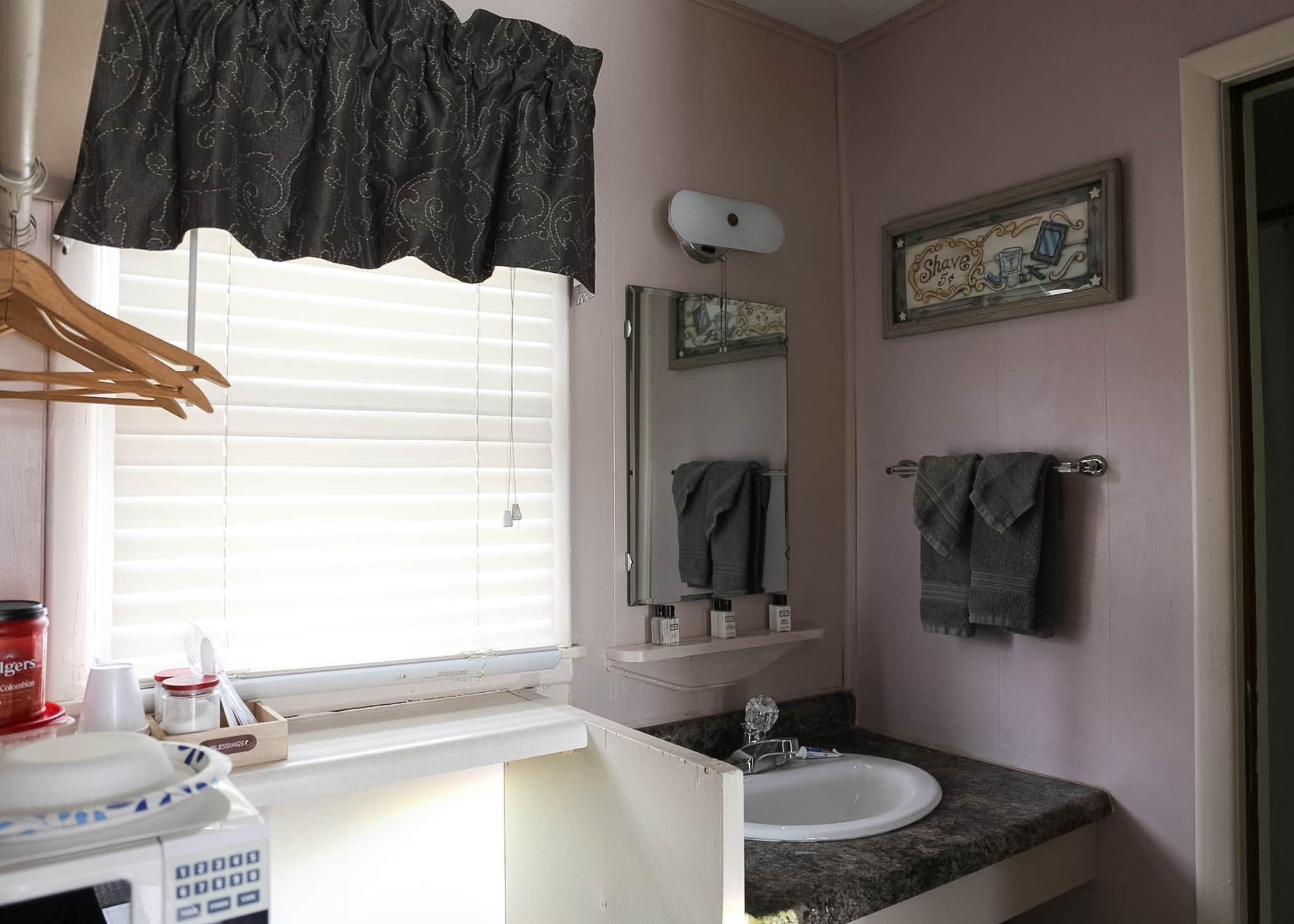 A bathroom with a window, sink, mirror, towel rack, and a framed picture on the wall.