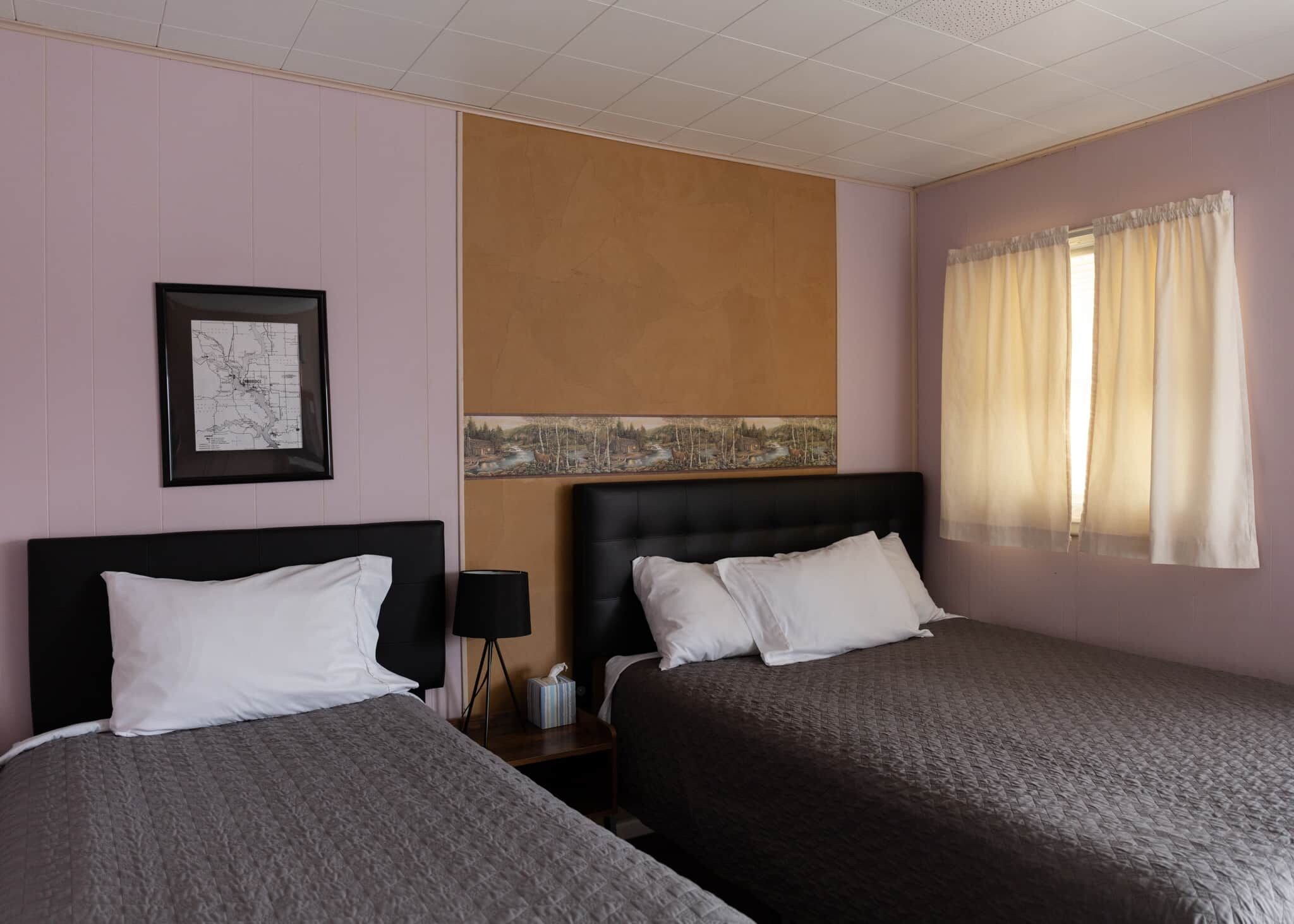 Une chambre d’hôtel avec deux lits, une table de chevet, une lampe et une fenêtre avec des rideaux.