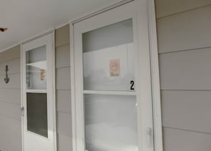 Une rangée de portes à cadre blanc, dotées de panneaux en verre dépoli, chacune étant munie d’un panneau indiquant « DÉFENSE DE FUMER » et d’un numéro.