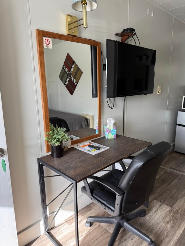 A room with a desk, chair, television, and a mirror.