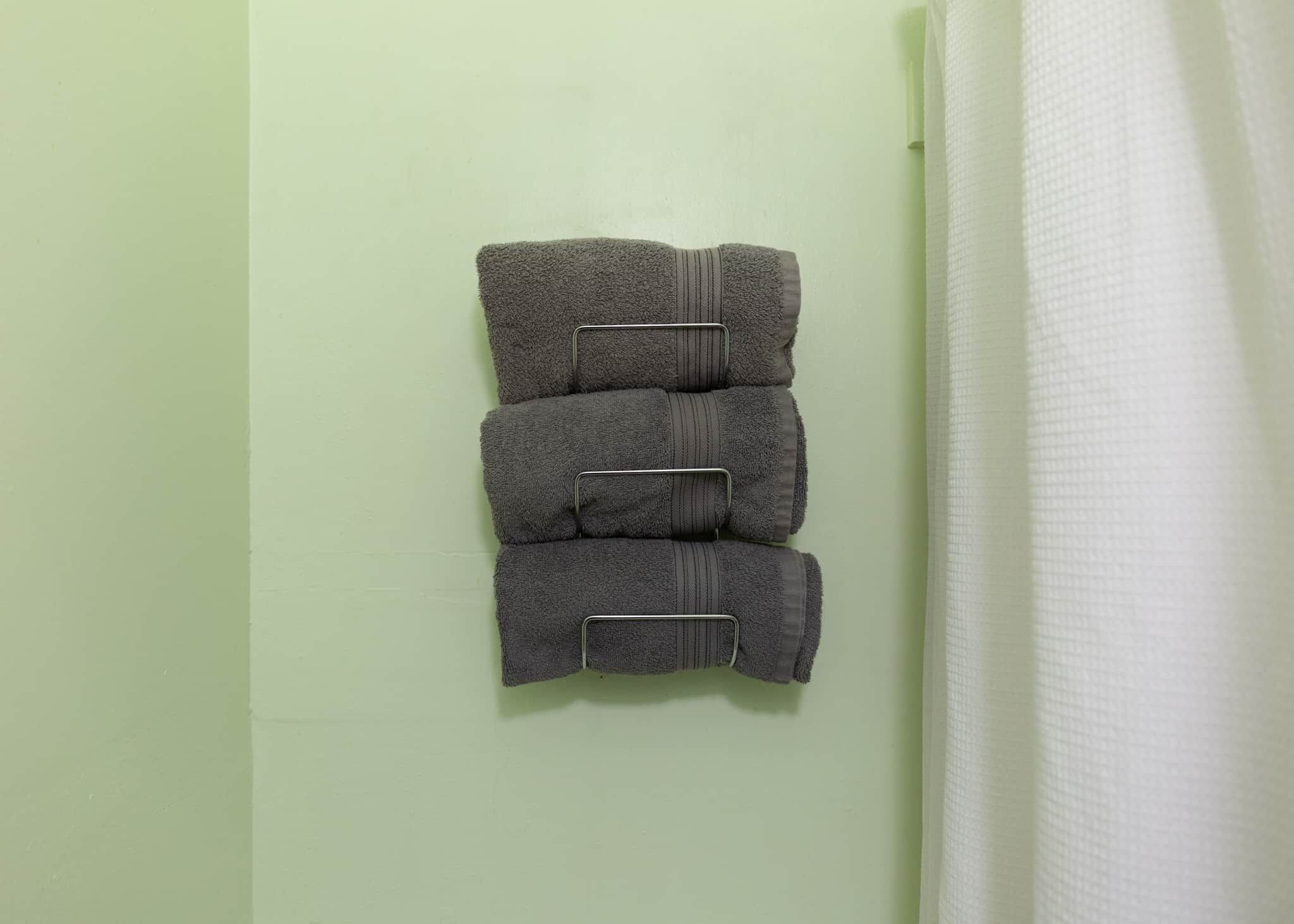 Een badkamer met een groene muur, een witte handdoek die rechts hangt en drie opgevouwen handdoeken op een handdoekhouder.