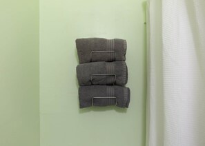 A bathroom with a green wall, a white towel hanging on the right, and three folded towels stacked on a towel rack.