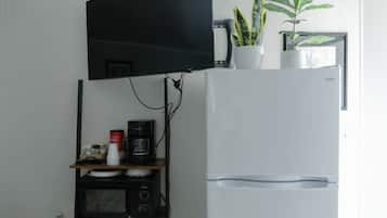 A kitchen with a flat-screen TV mounted above a microwave, a coffee maker, and a refrigerator with a water dispenser.