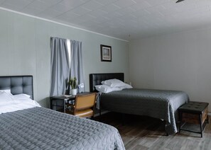 A hotel room with two beds, a desk, a chair, a potted plant, and a framed picture on the wall. - Motel Room 4 – 2 Queens + Twin (Mobridge)
